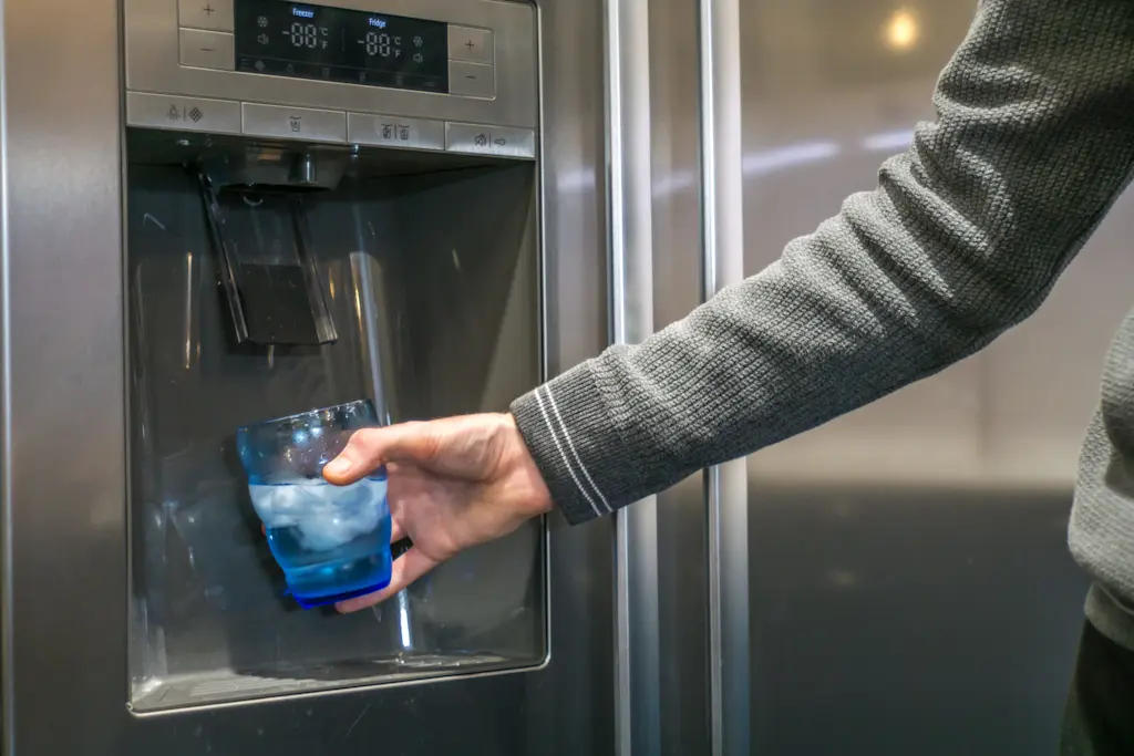 Person filling a glass at a refrigerator ice and water dispenser.