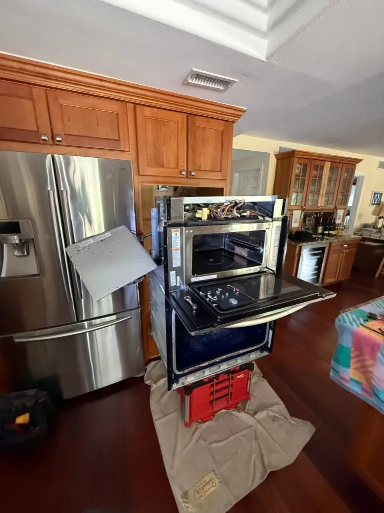 Professional microwave repair technician removing control panel from built-in microwave in modern kitchen