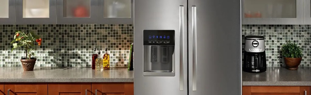 Modern stainless steel refrigerator with a digital water dispenser in a clean, upscale kitchen with mosaic tile backsplash.